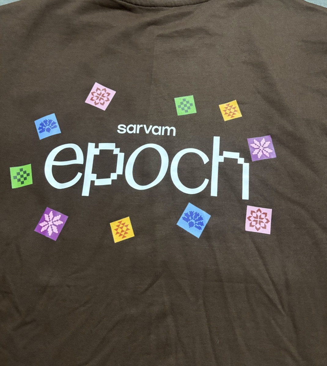 Brown Sarvam Epoch t-shirt with the pixel-art epoch logo and colorful tapestry tiles